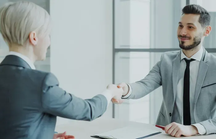 Professional man and woman shaking hands across a desk during a formal business meeting in a bright office